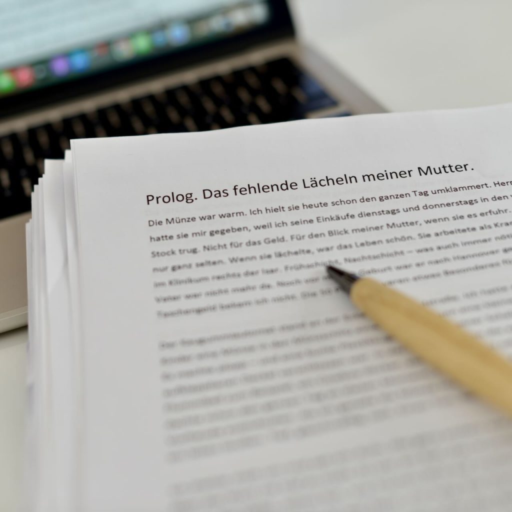 Gedrucktes Manuskript mit Prolog-Seite auf einem Schreibtisch neben einem Laptop und einem Stift.
